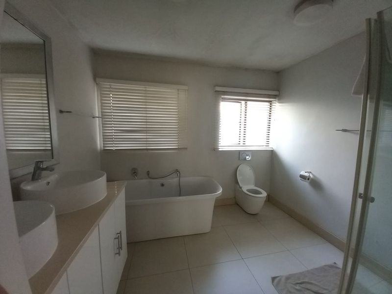 Modern bathroom featuring a double vanity, a sleek freestanding bathtub, a wall-mounted toilet, and a separate shower enclosure with neutral tiled flooring.