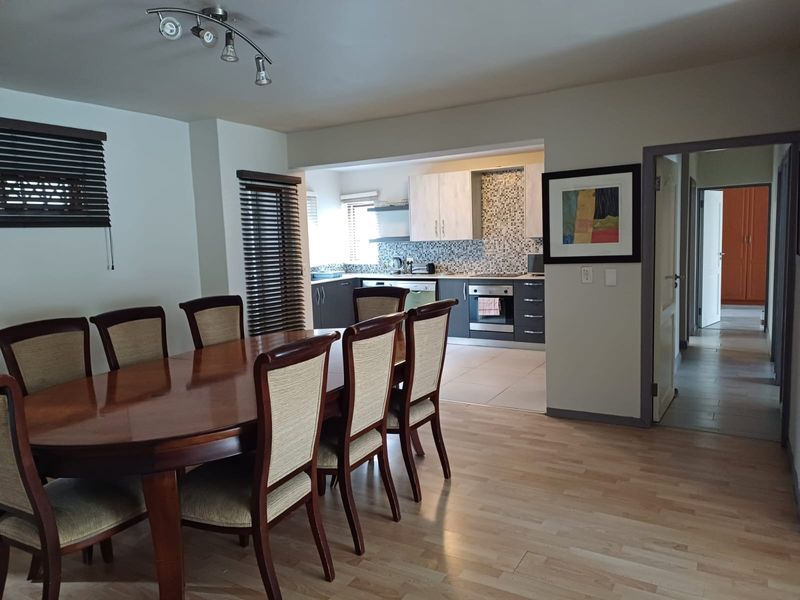 Open-plan dining area flowing into a modern kitchen featuring built-in cabinetry, mosaic backsplash, and integrated appliances with laminate flooring throughout.