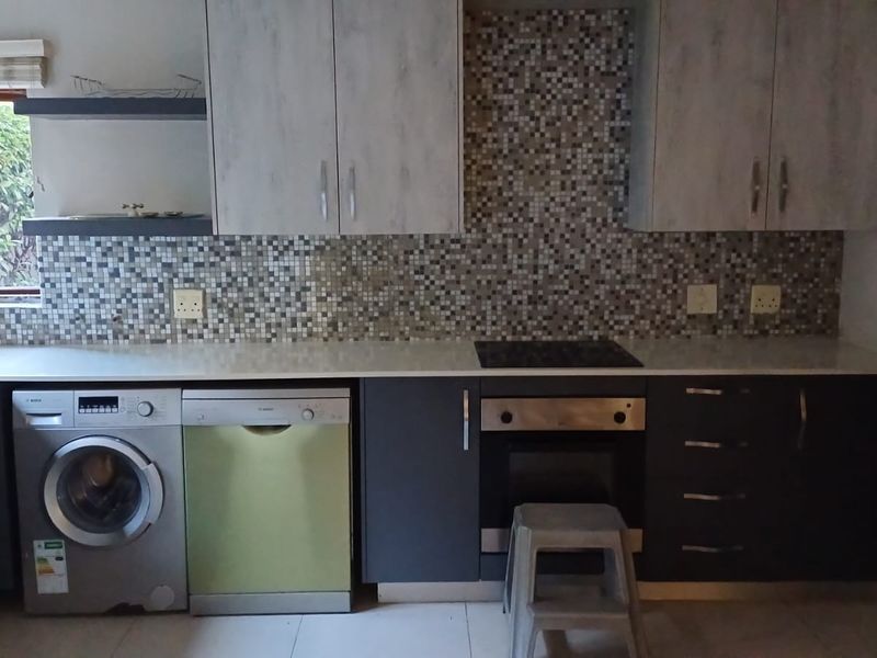 Modern kitchen featuring two-tone cabinetry, mosaic tile backsplash, integrated appliances, and a built-in oven and hob setup.