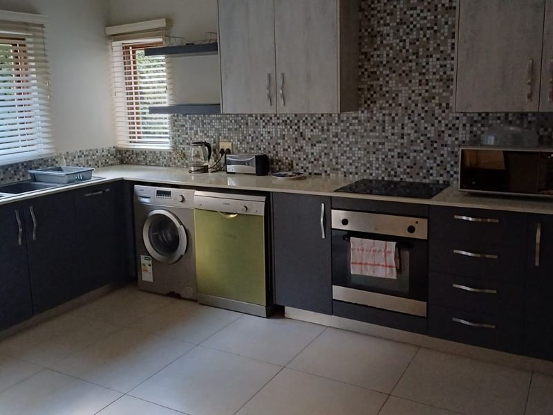 A functional kitchen featuring modern dark cabinetry, a mosaic tile backsplash, integrated oven and cooktop, and tiled flooring with ample natural light.