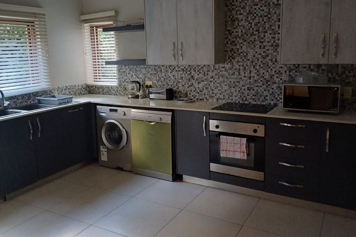A functional kitchen featuring modern dark cabinetry, a mosaic tile backsplash, integrated oven and cooktop, and tiled flooring with ample natural light.