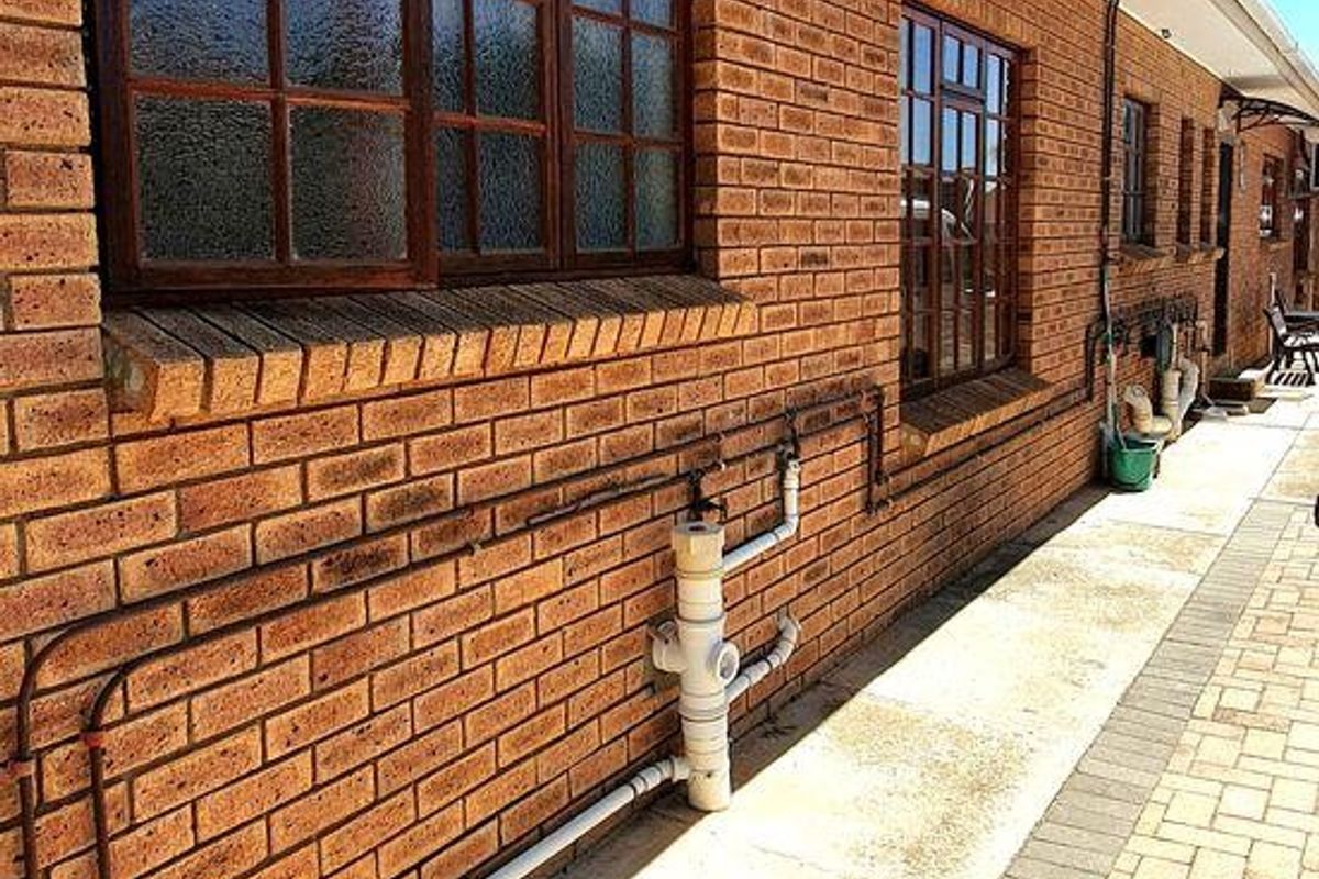 A side view of the property featuring a brick facade, timber-framed windows, and a paved walkway with visible external plumbing infrastructure.