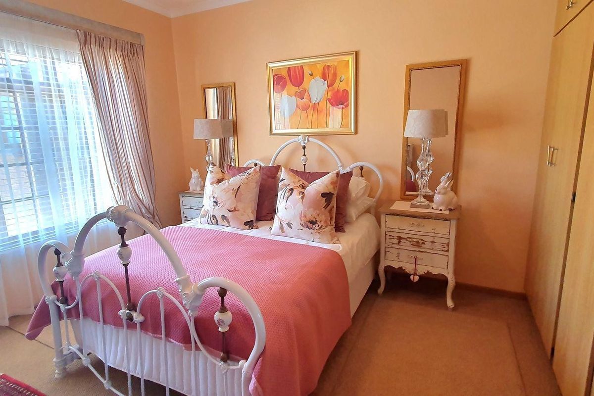 A cozy bedroom featuring built-in wooden cupboards, carpeted flooring, and large windows with blinds, offering a warm and functional living space.