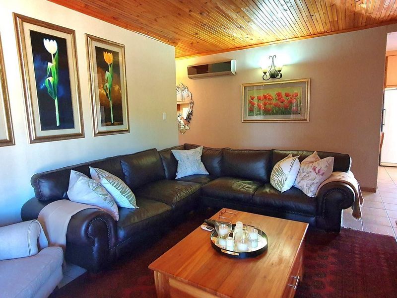 A comfortable living room featuring a warm timber tongue and groove ceiling, wall-mounted air conditioning, and tiled flooring leading to an adjacent area.