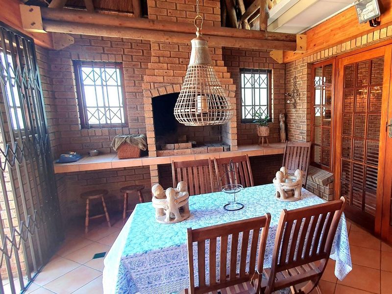 A covered patio area featuring a built-in brick fireplace, exposed timber ceiling beams, and tiled flooring, providing a rustic outdoor entertainment space.