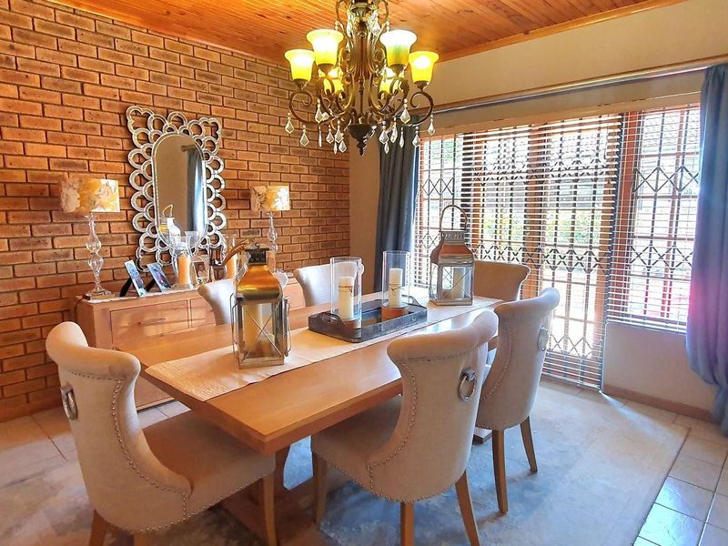 A dining room featuring an exposed brick feature wall, timber ceiling, and tiled flooring, illuminated by a traditional chandelier.