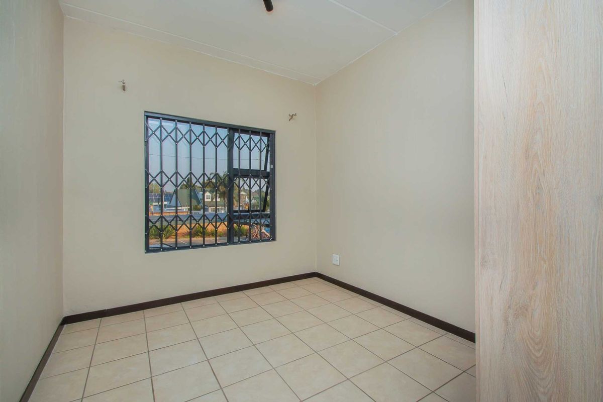 A clean, empty bedroom featuring neutral tiled flooring, a built-in cupboard, and a window fitted with a security gate.