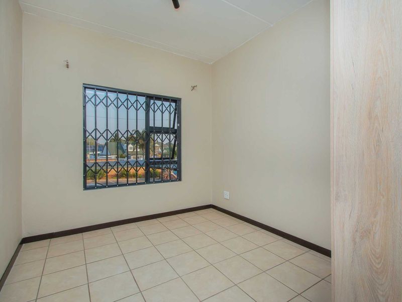 A clean, empty bedroom featuring neutral tiled flooring, a built-in cupboard, and a window fitted with a security gate.