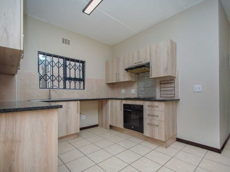 A clean, functional kitchen featuring light wood-finish cabinetry, granite countertops, built-in oven with extractor fan, and neutral tiled flooring.