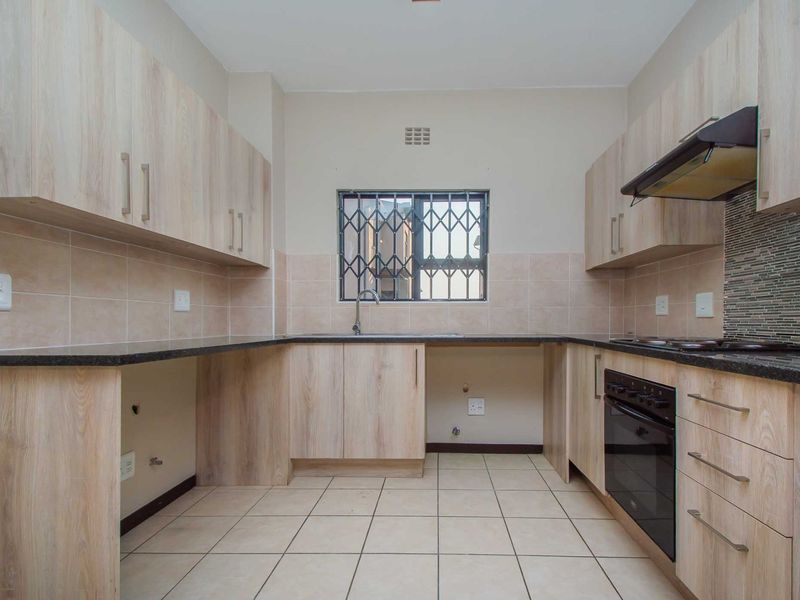 A clean, functional kitchen featuring light wood-finish cabinetry, granite countertops, built-in oven, hob, extractor fan, and tiled flooring.