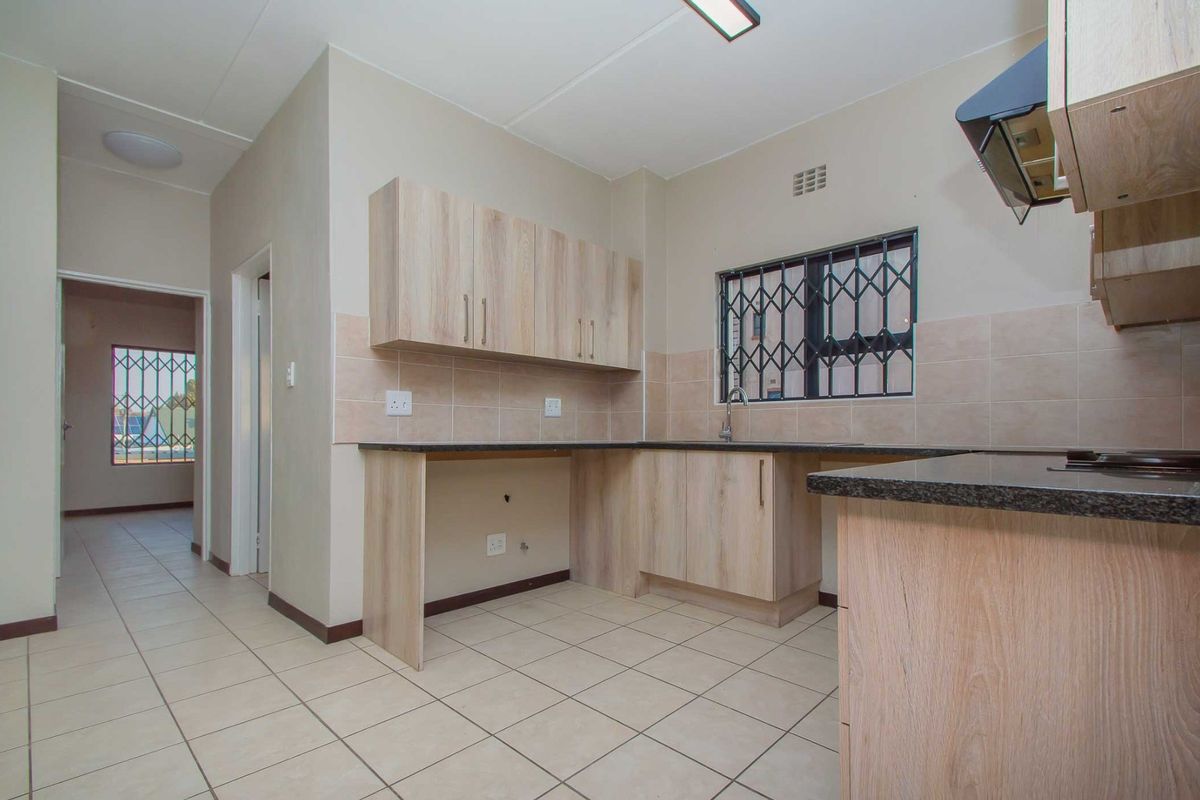 A functional kitchen featuring light wood-finish cabinetry, granite countertops, tiled backsplash, and tiled flooring, with a security gate installed on the window.