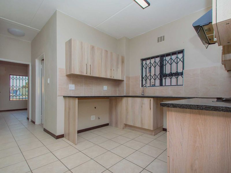 A functional kitchen featuring light wood-finish cabinetry, granite countertops, tiled backsplash, and tiled flooring, with a security gate installed on the window.
