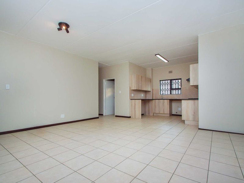 Spacious open-plan living area featuring neutral tiled flooring and a functional kitchen with built-in cabinetry and laminate countertops.
