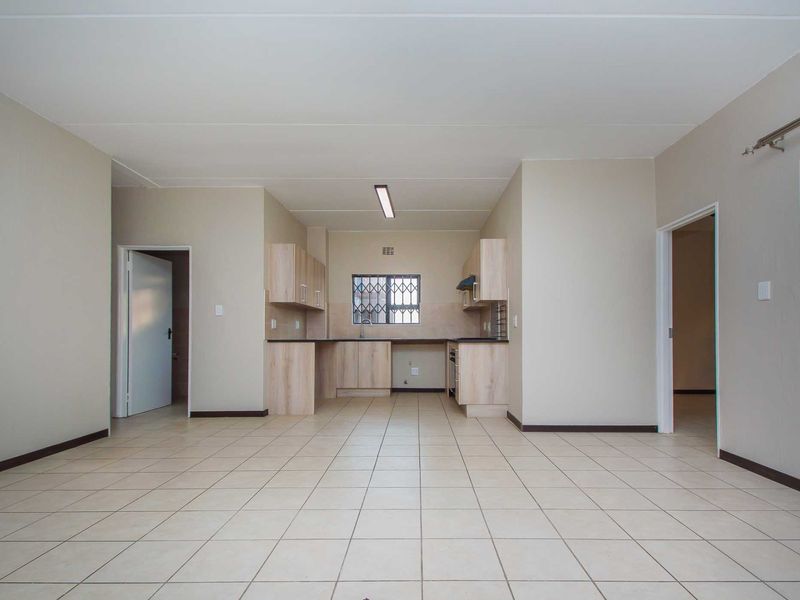 Spacious open-plan living area featuring neutral tiled flooring and a functional kitchen with built-in cabinetry and integrated appliances.