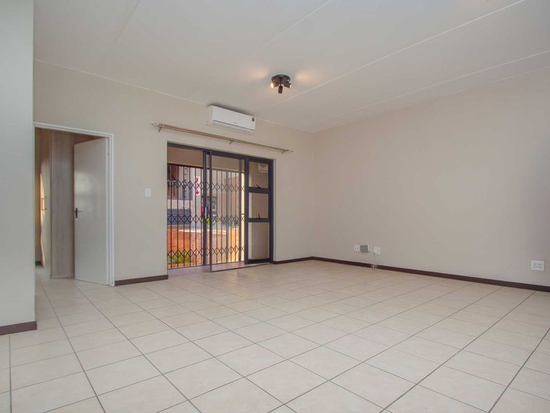 A spacious, empty living room featuring neutral tiled flooring, a wall-mounted air conditioning unit, and a sliding door leading to an outdoor area.