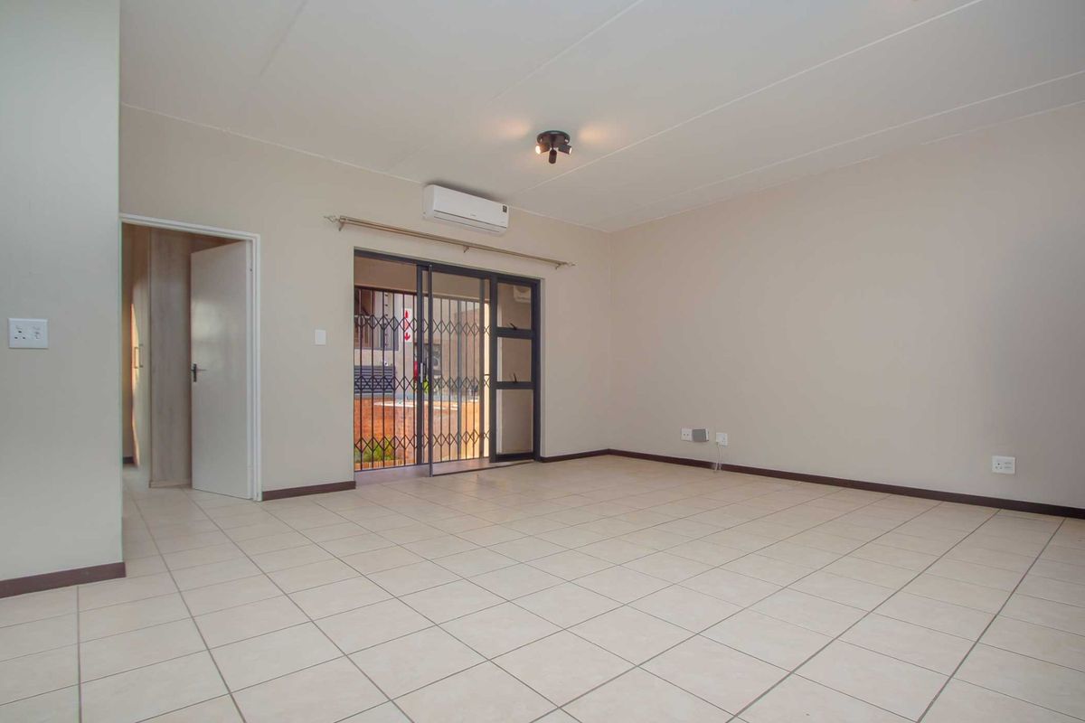 A spacious, empty living room featuring neutral tiled flooring, a wall-mounted air conditioning unit, and a sliding door leading to an outdoor area.