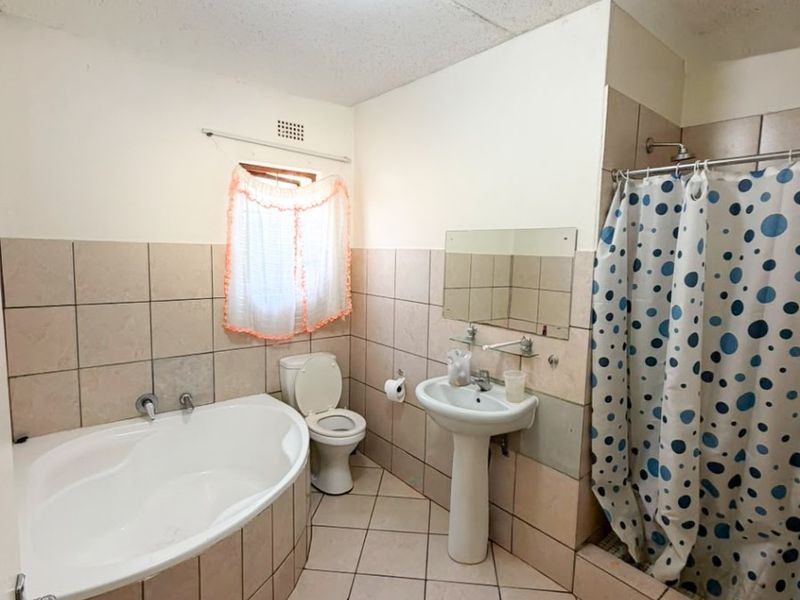 A dated bathroom featuring a corner bathtub, pedestal basin, toilet, and a shower enclosure with tiled walls and flooring.