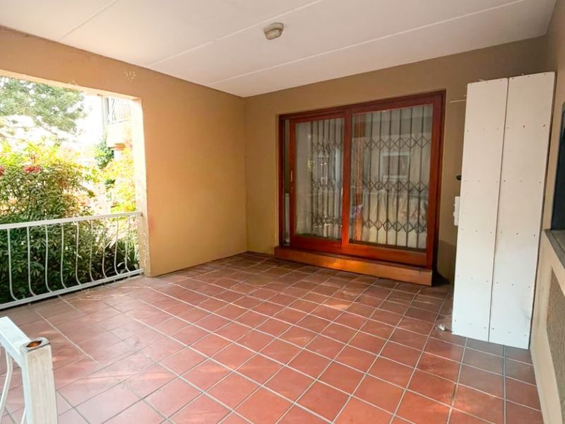 A covered patio area featuring terracotta-style floor tiles, a sliding glass door with security gate, and a metal balustrade overlooking the garden.