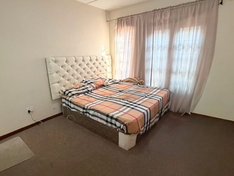 A standard bedroom featuring carpeted flooring, a ceiling light fixture, and a window with curtain rod installation.