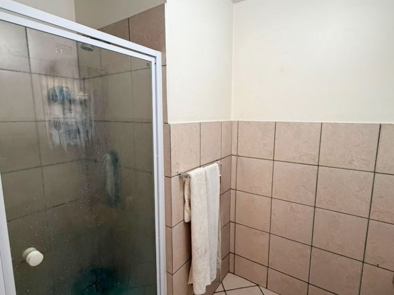 A functional bathroom featuring a shower enclosure with tiled walls and flooring, requiring some maintenance and cosmetic updates.