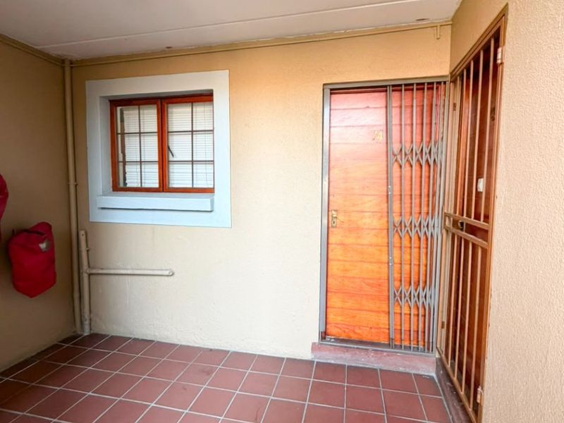 Covered entrance area featuring tiled flooring, a secure wooden door with a metal security gate, and a window with burglar bars.