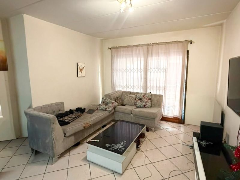 A living room featuring ceramic tiled flooring, a ceiling light fixture, and a sliding glass door with an integrated security gate.