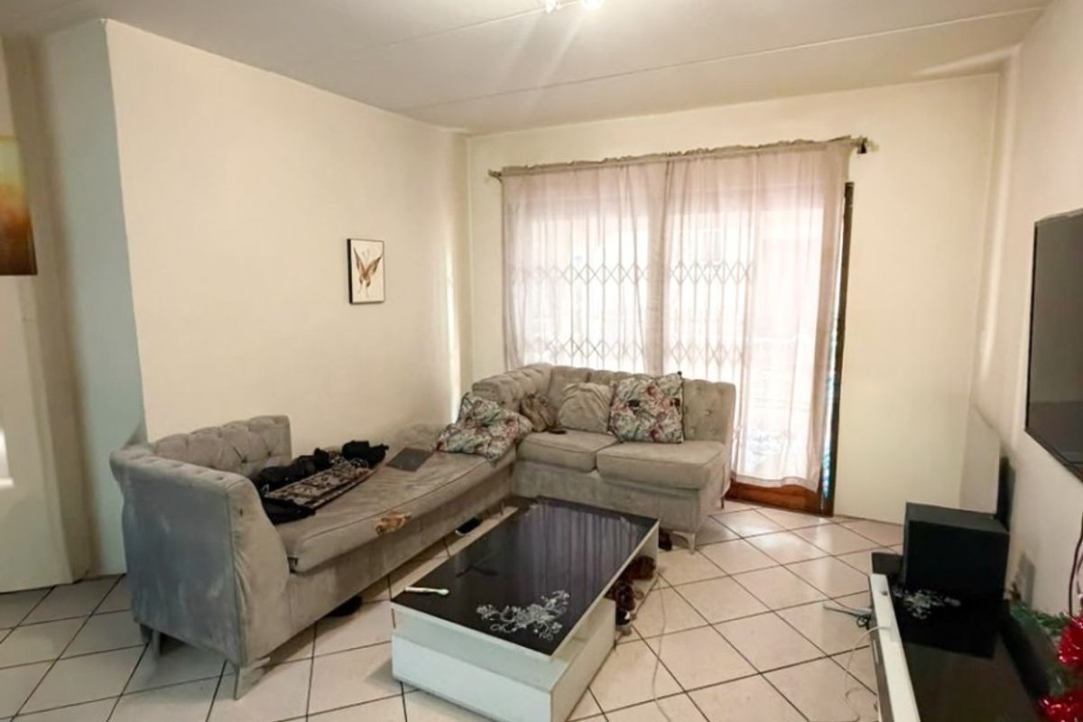 A living room featuring ceramic tiled flooring, a ceiling light fixture, and a sliding glass door with an integrated security gate.