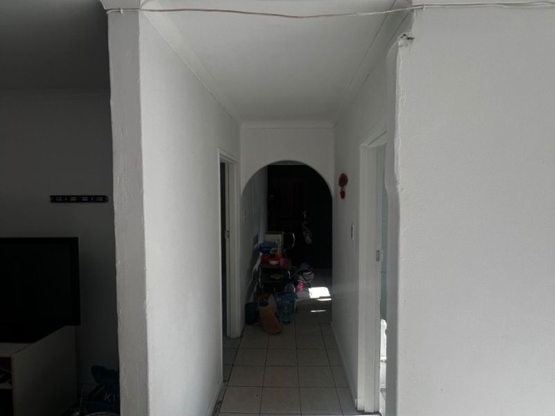A narrow hallway featuring tiled flooring and an arched transition, showing signs of wear including exposed wiring and damaged plasterwork.