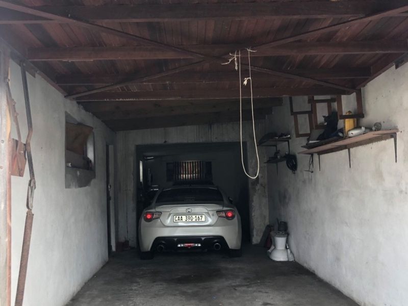 A functional garage space featuring an exposed timber ceiling, concrete flooring, and wall-mounted storage shelving.
