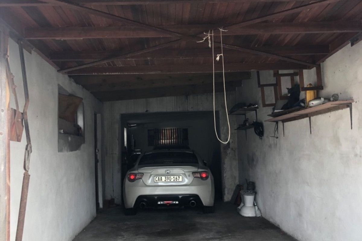 A functional garage space featuring an exposed timber ceiling, concrete flooring, and wall-mounted storage shelving.