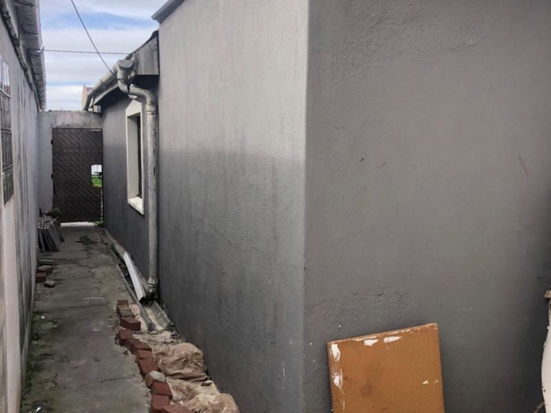 A narrow side passage featuring a concrete walkway, exterior wall with visible cracking, and basic drainage infrastructure along the side of the property.