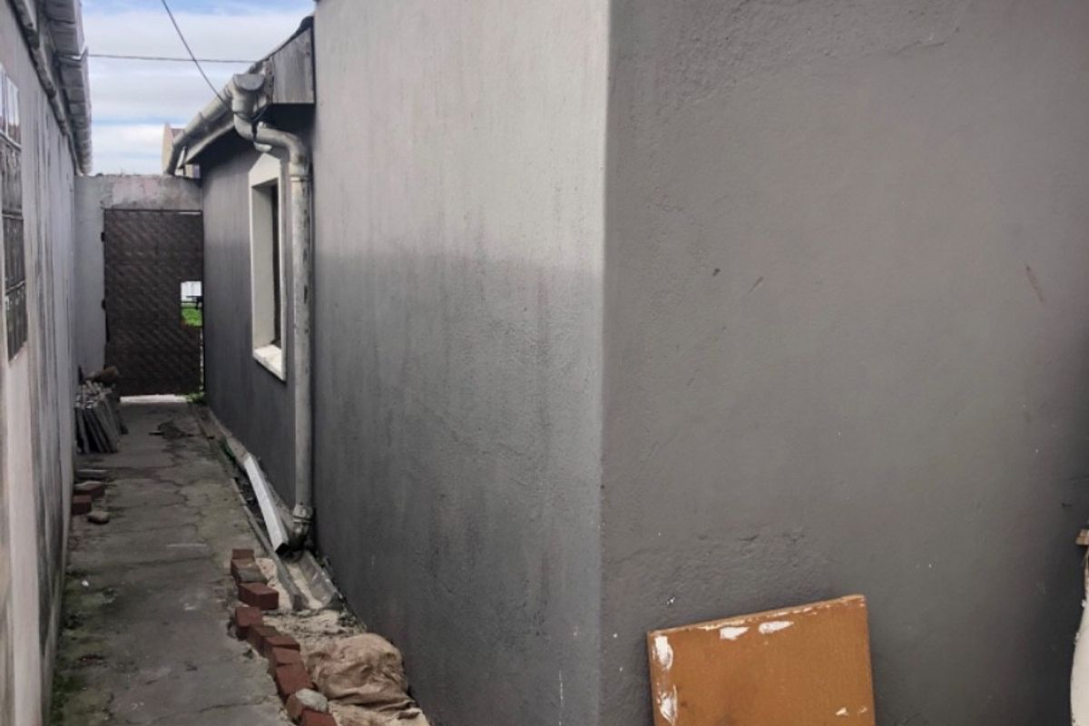 A narrow side passage featuring a concrete walkway, exterior wall with visible cracking, and basic drainage infrastructure along the side of the property.