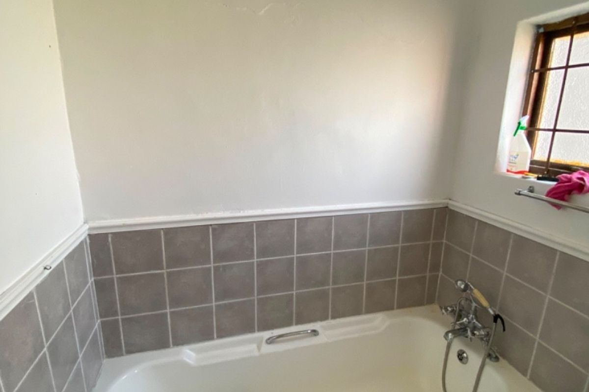 A dated bathroom featuring a built-in bathtub with chrome fixtures and neutral wall tiling, requiring cosmetic updates to improve its overall appeal.