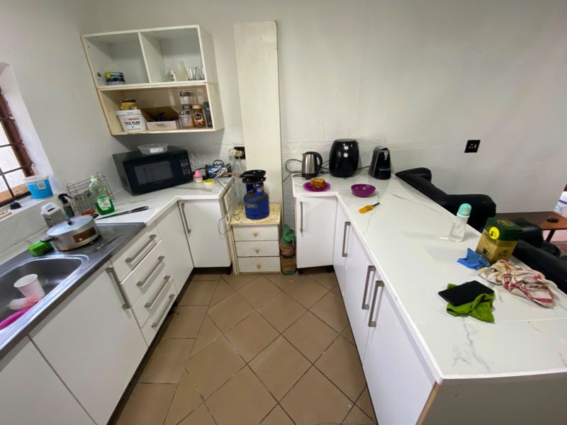 A compact kitchen featuring white cabinetry, stone countertops, and tiled flooring, requiring minor finishing touches to complete the installation.
