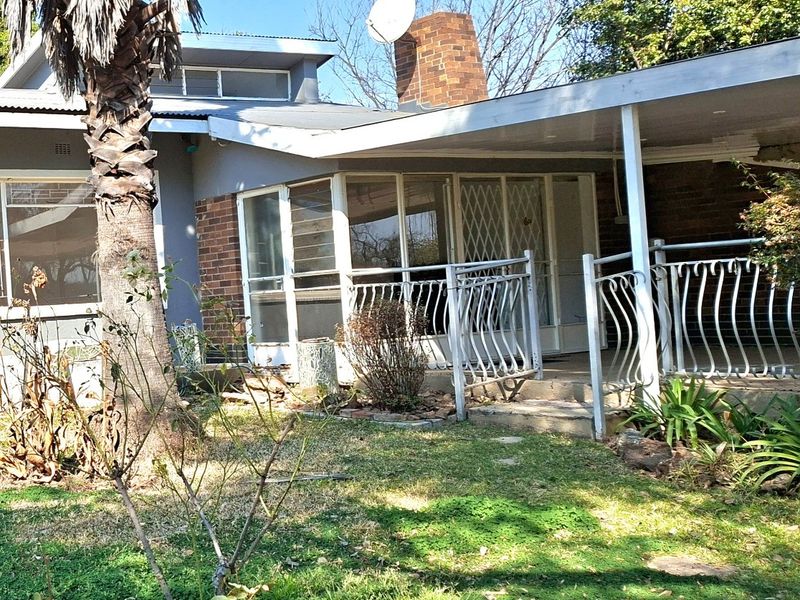 Rear view of the house featuring a covered patio area, brick chimney, and metal security features, set within a garden space.