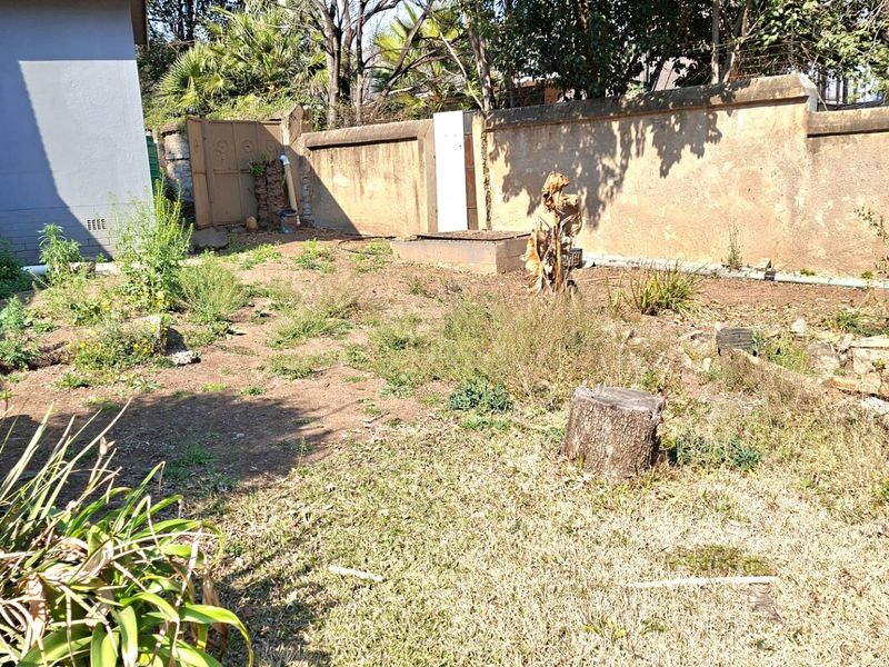 A rear garden area featuring a perimeter boundary wall and metal gate, currently requiring landscaping and maintenance to improve the outdoor space.