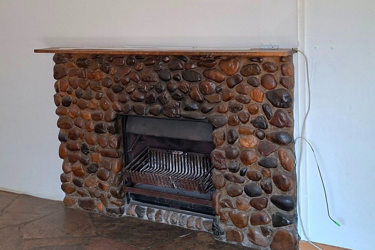A living room featuring a rustic stone fireplace with a wooden mantelpiece and traditional flagstone flooring.