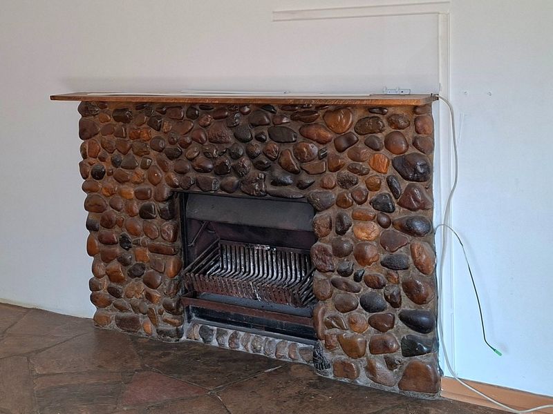 A living room featuring a rustic stone fireplace with a wooden mantelpiece and traditional flagstone flooring.