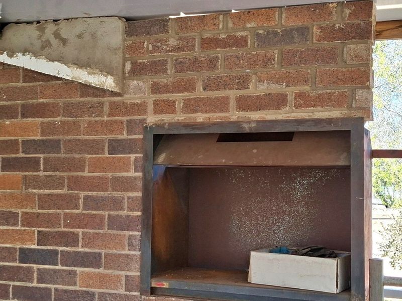 Outdoor patio area featuring a built-in brick braai unit, currently showing signs of unfinished construction and wear.