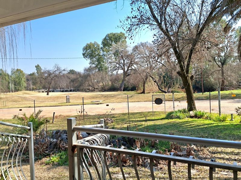 A view from a covered patio overlooking a grassy landscape and mature trees.