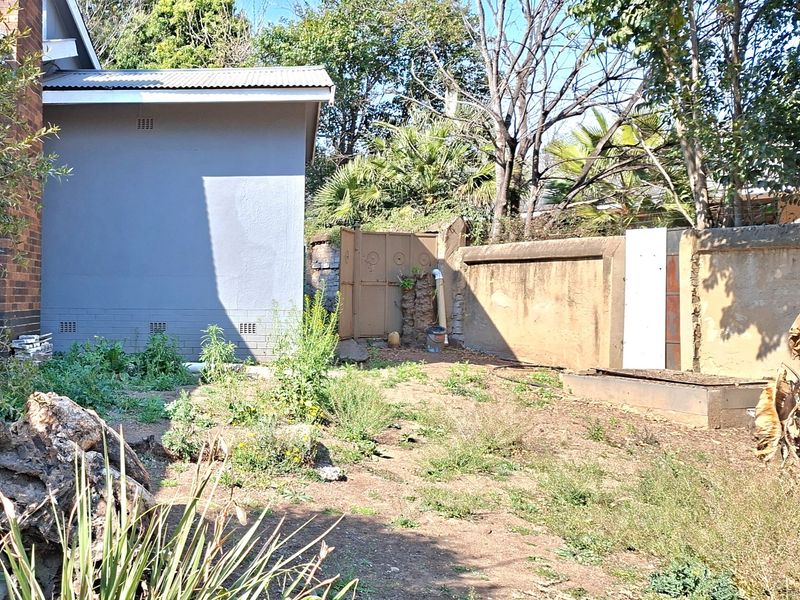 Rear garden area featuring a brick building facade, boundary wall, and metal gate, requiring landscaping and maintenance.