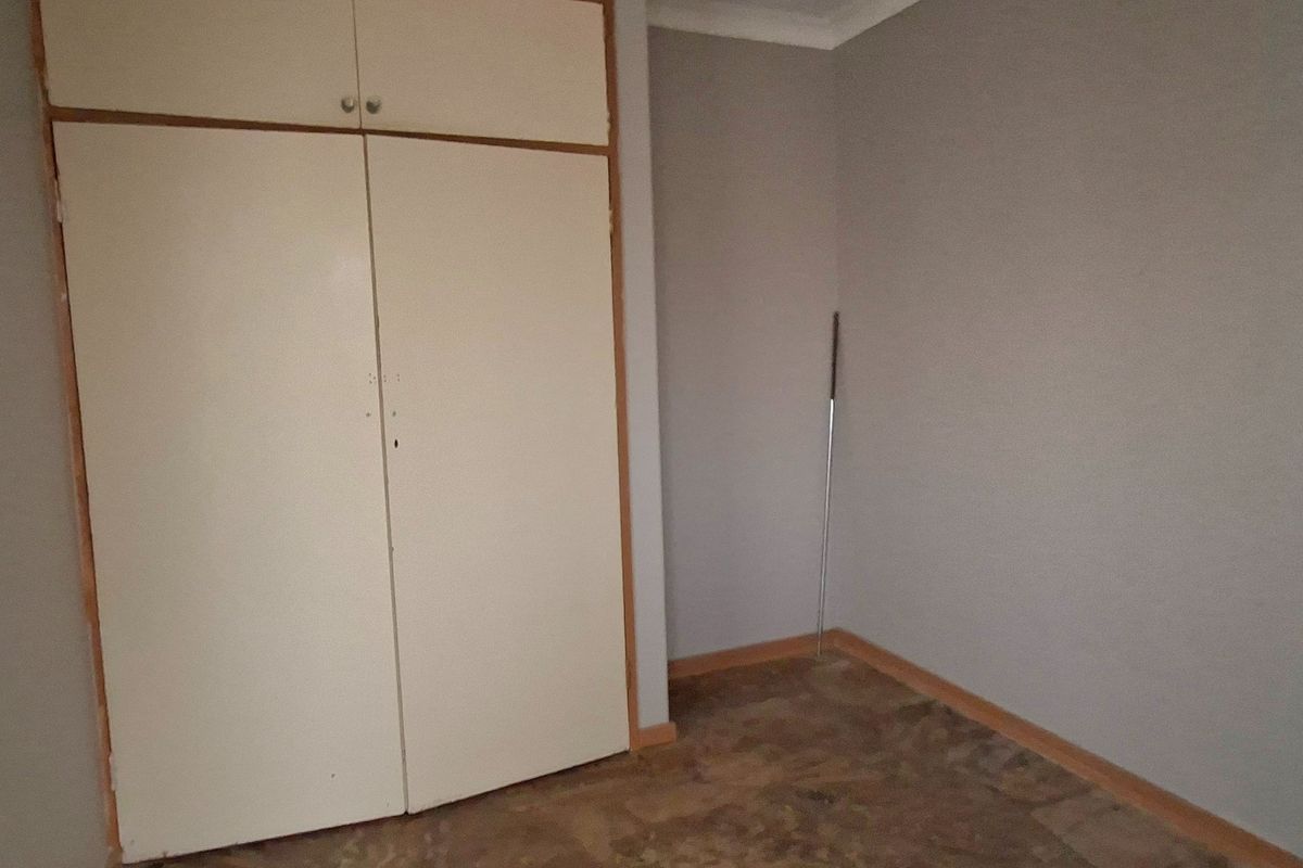 An empty bedroom featuring built-in cupboards, cove cornicing, and stone-look flooring, offering a blank canvas for renovation.