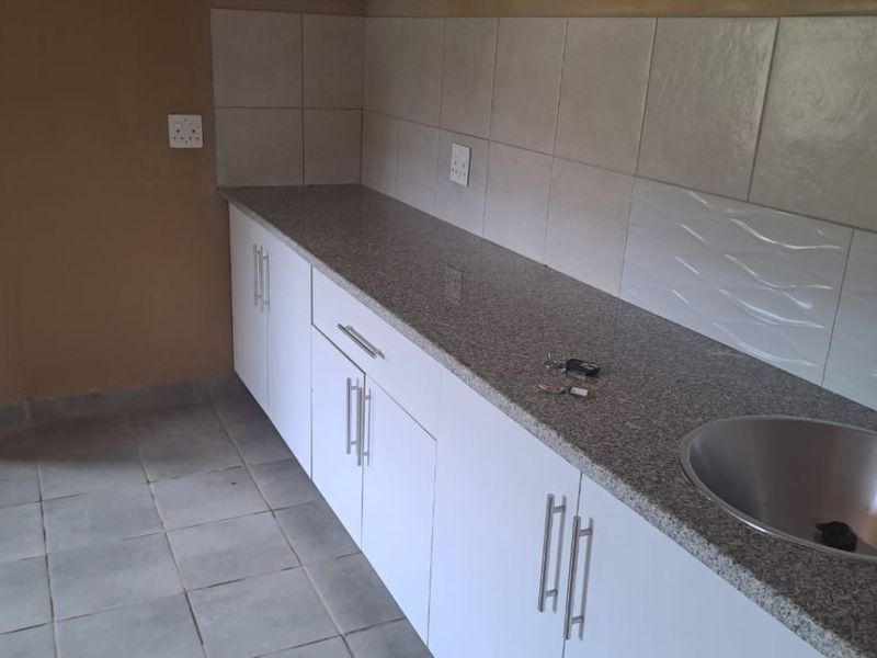 A functional kitchen area featuring granite countertops, white cabinetry, and a stainless steel sink, ready for final finishing touches.