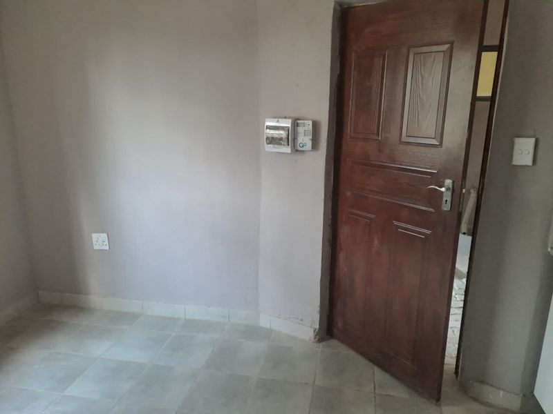 A functional hallway area featuring tiled flooring, a solid timber door, and wall-mounted electrical and security infrastructure.