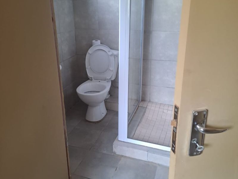 A compact bathroom featuring a shower enclosure and toilet with neutral wall and floor tiling, currently requiring finishing touches to the door frame.