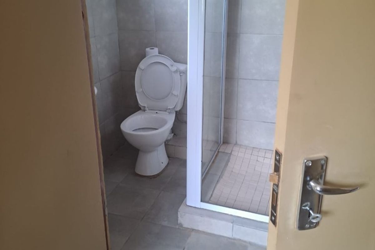 A compact bathroom featuring a shower enclosure and toilet with neutral wall and floor tiling, currently requiring finishing touches to the door frame.