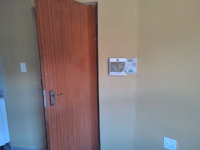A functional hallway area featuring a timber door, wall-mounted alarm system, and electrical distribution board.