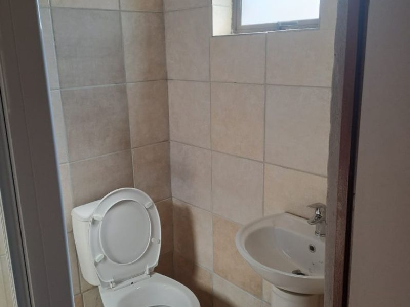 A compact guest bathroom featuring a pedestal basin, toilet, and neutral wall tiling with a small frosted window for natural light.
