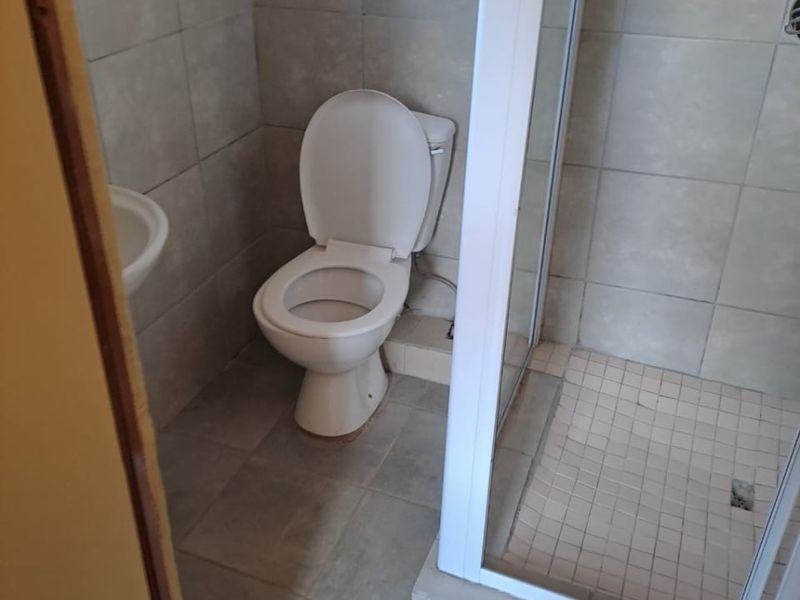 A functional bathroom featuring a shower enclosure, toilet, and pedestal basin with neutral wall and floor tiling.