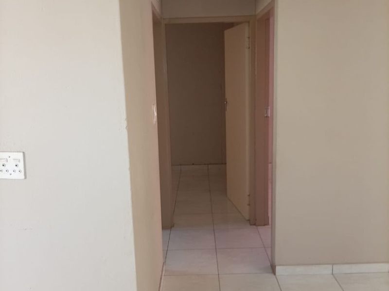 A clean, neutral-toned hallway featuring tiled flooring and a ceiling access hatch, providing a simple transition between rooms.